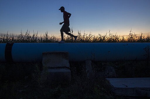 A man running on top of a sewage pipe at Katlehong, east of Johannesburg, South Africa, Tuesday, March 24, 2020, a day after it was announced that South Africa will go into a nationwide lockdown for 21 days from Thursday to fight the spread of the new coronavirus. The highly contagious COVID-19 coronavirus can cause mild symptoms, but for some it can cause severe illness including pneumonia. (AP Photo/Themba Hadebe)