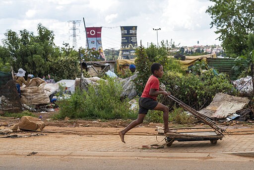 A young boy rides a cart used to carry refuse bags in an informal settlement of Soweto, South Africa, Wednesday March 25, 2020. South Africa will go into a nationwide lockdown for 21 days starting Friday morning, in an effort to control the spread to the coronavirus. The new coronavirus causes mild or moderate symptoms for most people, but for some, especially older adults and people with existing health problems, it can cause more severe illness or death. (AP Photo/Jerome Delay)