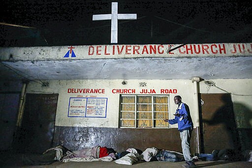 In this photo taken Tuesday, March 24, 2020, a drunk homeless person preaches to others as they sleep on the street outside a church in the Mathare slum, or informal settlement, of Nairobi, Kenya. Many slum residents say staying at home or social-distancing is impossible for those who live hand to mouth, receiving daily wages for informal work with no food or economic assistance from the government, as is maintaining sanitation where a pit latrine can be shared by over 50 people. The new coronavirus causes mild or moderate symptoms for most people, but for some, especially older adults and people with existing health problems, it can cause more severe illness or death. (AP Photo/Brian Inganga)