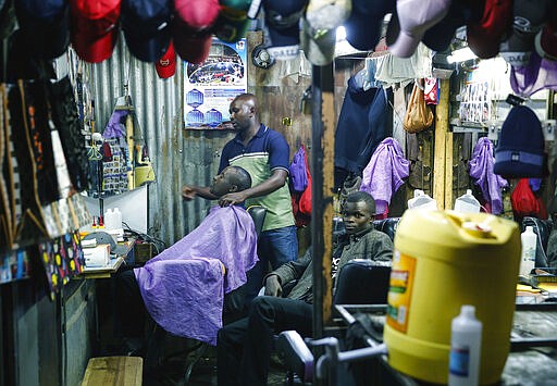 In this photo taken Tuesday, March 24, 2020, a barber continues his trade despite the fear of the new coronavirus, saying &quot;It's better to die sick than die hungry&quot;, in the Mathare slum, or informal settlement, of Nairobi, Kenya. Many slum residents say staying at home or social-distancing is impossible for those who live hand to mouth, receiving daily wages for informal work with no food or economic assistance from the government, as is maintaining sanitation where a pit latrine can be shared by over 50 people. The new coronavirus causes mild or moderate symptoms for most people, but for some, especially older adults and people with existing health problems, it can cause more severe illness or death. (AP Photo/Brian Inganga)