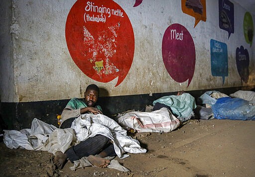 In this photo taken Tuesday, March 24, 2020, a homeless man prepares to sleep next to others on the side of a road in the Mathare slum, or informal settlement, of Nairobi, Kenya. Many slum residents say staying at home or social-distancing is impossible for those who live hand to mouth, receiving daily wages for informal work with no food or economic assistance from the government, as is maintaining sanitation where a pit latrine can be shared by over 50 people. The new coronavirus causes mild or moderate symptoms for most people, but for some, especially older adults and people with existing health problems, it can cause more severe illness or death. (AP Photo/Brian Inganga)