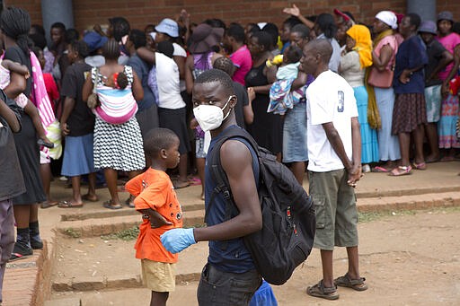 A man wearing a mask is seen near a food queue in Harare, Zimbabwe, Wednesday, March 25, 2020. 
Zimbabwe's public hospital doctors went on strike Wednesday over what they called a lack of adequate protective gear as the coronavirus begins to spread in a country whose health system has almost collapsed.  The new coronavirus causes mild or moderate symptoms for most people, but for some, especially older adults and people with existing health problems, it can cause more severe illness or death.(AP Photo/Tsvangirayi Mukwazhi)