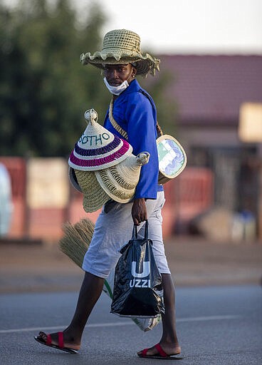 A man wearing a mask, sells traditional hats on the street in Daveyton, east of Johannesburg, South Africa, Tuesday, March 24, 2020, a day after it was announced that South Africa will go into a nationwide lockdown for 21 days from Thursday to fight the spread of the new coronavirus. For most people the virus causes only mild or moderate symptoms. For others it can cause more severe illness, especially in older adults and people with existing health problems. (AP Photo/Themba Hadebe)