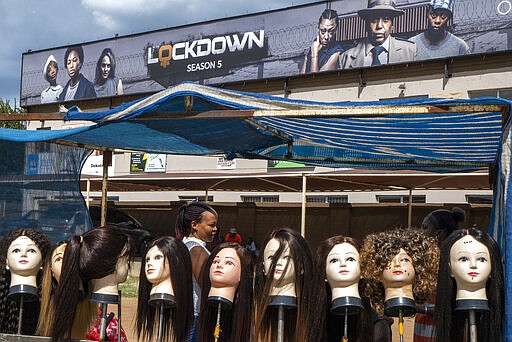 Wigs are sold under an advert for a popular television series in the township of Soweto, outside Johannesburg, South Africa, Wednesday March 25, 2020. South Africa will go into a nationwide lockdown for 21 days starting Friday morning, in an effort to mitigate the spread to the coronavirus. The new coronavirus causes mild or moderate symptoms for most people, but for some, especially older adults and people with existing health problems, it can cause more severe illness or death. (AP Photo/Jerome Delay)