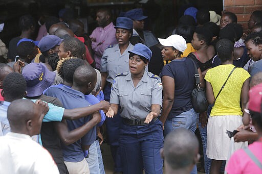 Zimbabwean police control a crowd that had gathered to buy maize meal at a supermarket in Harare, Zimbabwe, Wednesday, March 25, 2020. Zimbabwe's public hospital doctors went on strike Wednesday over what they called a lack of adequate protective gear as the coronavirus begins to spread in a country whose health system has almost collapsed.  The new coronavirus causes mild or moderate symptoms for most people, but for some, especially older adults and people with existing health problems, it can cause more severe illness or death. (AP Photo/Tsvangirayi Mukwazhi)