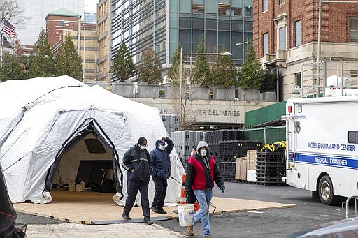 Medical Examiner personnel and construction workers are seen at the site of a makeshift morgue being built in New York, Wednesday, March 25, 2020. The number of people hospitalized with COVID-19 in New York climbed to 3,800, with close to 900 in intensive care, with the peak of the outbreak weeks away, Gov. Andrew Cuomo said Wednesday. The new coronavirus causes mild or moderate symptoms for most people, but for some, especially older adults and people with existing health problems, it can cause more severe illness or death. (AP Photo/Mary Altaffer)