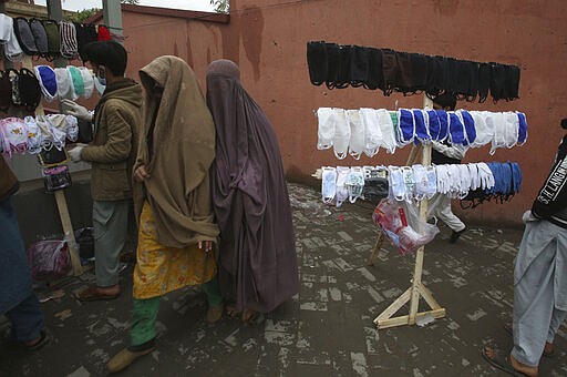 Pakistani women walk past vendors selling face masks to prevent the spread of the coronavirus, in Peshawar, Pakistan, Tuesday, March 24, 2020. Pakistani authorities said they'd shut down train operations across the country from Wednesday until March 31 in an effort to contain the spread of the virus. (AP Photo/Muhammad Sajjad)