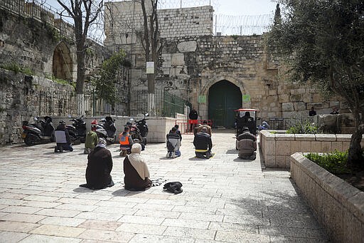 People pray in front of the shuttered gates to al-Aqsa mosque compound as all prayers are suspended to prevent the spread of coronavirus in Jerusalem, Monday, March 23, 2020. In Israel daily life has largely shut down with coronavirus cases multiplying greatly over the past week, (AP Photo/Mahmoud Illean)