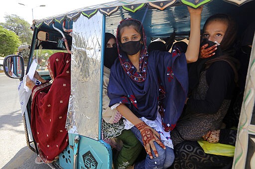 People traveling in a motorized rickshaw wear face masks in an effort to avoid the spread of the coronavirus, in Karachi, Pakistan, Tuesday, March 24, 2020. Pakistani authorities said they'd shut down train operations across the country from Wednesday until March 31 in an effort to contain the spread of the virus. (AP Photo/Fareed Khan)