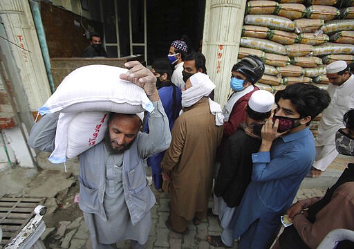 People buy sacks of flour fearing a shortage due to the coronavirus outbreak, in Peshawar, Pakistan, Tuesday, March 24, 2020. Pakistani authorities meanwhile said they'd shut down train operations across the country from Wednesday until March 31 in an effort to contain the spread of the virus. (AP Photo/Muhammad Sajjad)