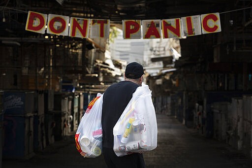 A man carries his shopping as he walks by a &quot;don't panic&quot; sign hanging at the entrance of a food market that is closed in order to reduce the spread of the coronavirus, in Tel Aviv, Israel, Monday, March 23, 2020. In Israel daily life has largely shut down with coronavirus cases multiplying greatly over the past week. (AP Photo/Oded Balilty)