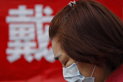 FILE - In this Wednesday, March 18, 2020, file photo, a woman wearing a protective face mask to prevent the new coronavirus outbreak walks by a propaganda poster with a word &quot;Wear&quot; outside a residential building in Beijing. World War II references are now heard daily, not because another momentous 75th anniversary, Victory in Europe Day approaches in May but because of the coronavirus. (AP Photo/Andy Wong, File)