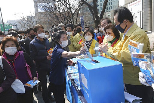 A woman puts an envelope containing a face mask into a charity box as South Korean Prime Minister Chung Se-kyun, right, watches during a campaign for the donation of face masks to impoverished people amid the spread of the new coronavirus in Seoul, South Korea, Wednesday, March 25, 2020. For most people, the new coronavirus causes mild or moderate symptoms, such as fever and cough that clear up in two to three weeks. For some, especially older adults and people with existing health problems, it can cause more severe illness, including pneumonia and death. (AP Photo/Ahn Young-joon)