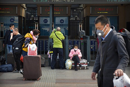 Travelers wearing face masks walk outside the Beijing Railway Station in Beijing, Wednesday, March 25, 2020. Some train stations and bus services reopened in China's Hubei Province on Wednesday and people who passed a health check would finally be allowed to travel for the first time since the coronavirus outbreak surged in January. (AP Photo/Mark Schiefelbein)