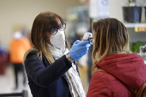 An employee test customers' body temperature at the entrance of the Esselunga supermarket, in Milan, Italy, Wednesday, March 25, 2020. The new coronavirus causes mild or moderate symptoms for most people, but for some, especially older adults and people with existing health problems, it can cause more severe illness or death. (AP Photo/Luca Bruno)