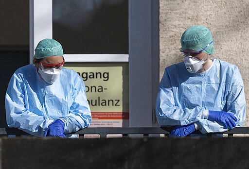 Employees of the Corona Outpatient Clinic at the University Hospital stand in protective clothing and breathing masks in front of the entrance, Dresden, Germany, Wedneday, March 25, 2020. To contain the corona virus, Saxony now bans all accumulations of three or more people in public. (Robert Michael/dpa via AP)