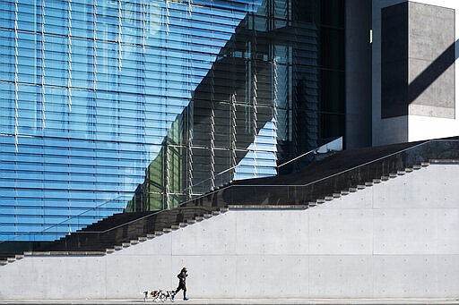 A lonely man runs with two dogs in front of a parliament building in the government district in Berlin, Germany, Wednesday, March 25, 2020. In order to slow down the spread of the coronavirus, the German government has considerably restricted public life and asked the citizens to stay at home. The new coronavirus causes mild or moderate symptoms for most people, but for some, especially older adults and people with existing health problems, it can cause more severe illness or death. (AP Photo/Markus Schreiber)