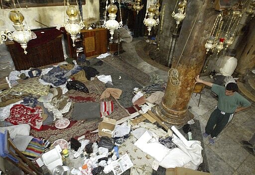 FILE - In this May 10, 2002 file photo, a Palestinian resident of Bethlehem looks over the remains of sleeping mats and food where those under siege inside the Church of the Nativity had been living. Western countries are reeling from the coronavirus pandemic, awakening to a new reality of economic collapse, overwhelmed hospitals and home confinement. But for millions across the Middle East and in conflict zones elsewhere, much of this is familiar. (AP Photo/David Guttenfelder, File)