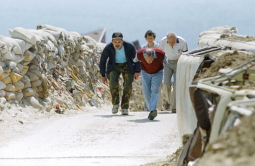 FILE - In this June 13, 1993 file photo, men run across the bridge into the Sarajevo suburb of Dobrinja in Sarajevo. The suburb was isolated from the capital for three months by Bosnian Serb forces. Western countries are reeling from the coronavirus pandemic, awakening to a new reality of economic collapse, overwhelmed hospitals and home confinement. But for millions across the Middle East and in conflict zones elsewhere, much of this is familiar. Survivors of recent conflicts offer wisdom, such as stocking up on essentials, helping your neighbors and knowing that others have gone through much worse. (AP Photo/Peter Northall, File)