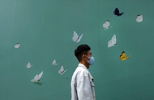 A man wearing face mask walks past a shop at a down town street in Hong Kong Wednesday, March 25, 2020. For most, the coronavirus causes only mild or moderate symptoms, such as fever and cough. But for a few, especially older adults and people with existing health problems, it can cause more severe illnesses, including pneumonia. (AP Photo/Vincent Yu)