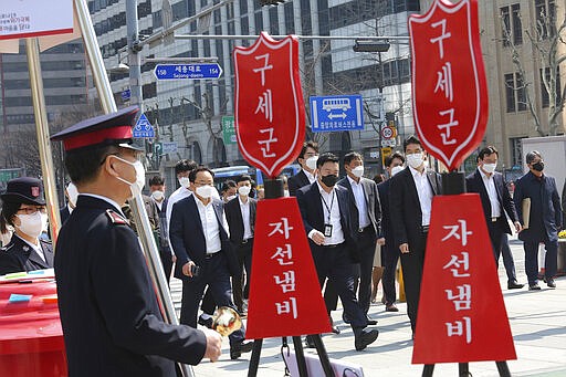 People wearing face masks pass members of the Salvation Army's campaign for the donation of face masks and money to impoverished people amid the spread of the new coronavirus in Seoul, South Korea, Wednesday, March 25, 2020. For most people, the new coronavirus causes only mild or moderate symptoms, such as fever and cough. For some, especially older adults and people with existing health problems, it can cause more severe illness, including pneumonia. The sign reads: &quot;The Salvation Army and charity pot.&quot; (AP Photo/Ahn Young-joon)