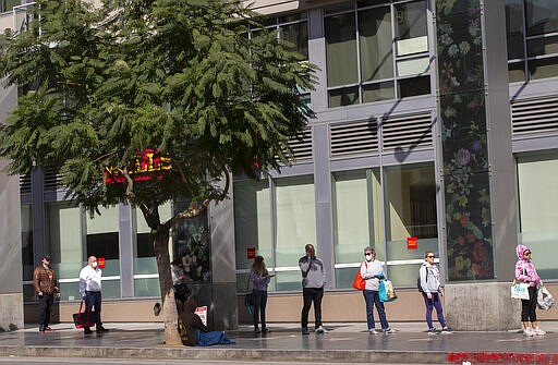 People stand in line, while maintaining distance to the neighboring person, as they wait to enter a Trader Joe's grocery store in the Hollywood section of Los Angeles on Tuesday, March 24, 2020. (AP Photo/Damian Dovarganes)