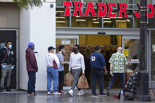 People stand in line, but leaving space to the neighboring person, while waiting to enter a Trader Joe's grocery store in the Hollywood section of Los Angeles on Tuesday, March 24, 2020. (AP Photo/Damian Dovarganes)