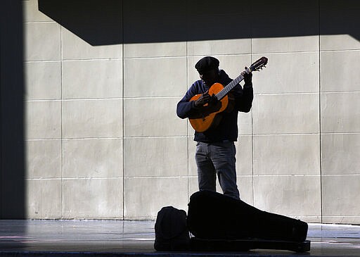 A lone street performer tunes his guitar on the deserted Hollywood Boulevard in Los Angeles on Tuesday, March 24, 2020. A tally by Johns Hopkins University on Tuesday found California coronavirus cases have topped 2,500, with at least 50 deaths. (AP Photo/Damian Dovarganes)