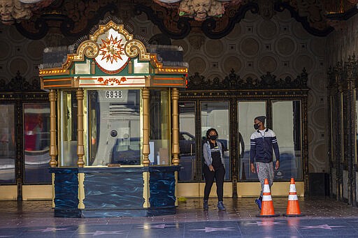 Tourists wearing masks look around the closed ticket booth of El Capitan Theatre, a normally packed tourist destination on Hollywood Boulevard in Los Angeles, Tuesday, March 24, 2020, as the U.S. continues to cope with the new coronavirus pandemic. (AP Photo/Damian Dovarganes)