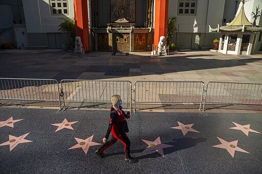 A pedestrian walks past the closed TCL Chinese Theatre, a normally packed tourist destination on Hollywood Boulevard in Los Angeles, Tuesday, March 24, 2020. New cases of the new coronavirus surged around the state. (AP Photo/Damian Dovarganes)