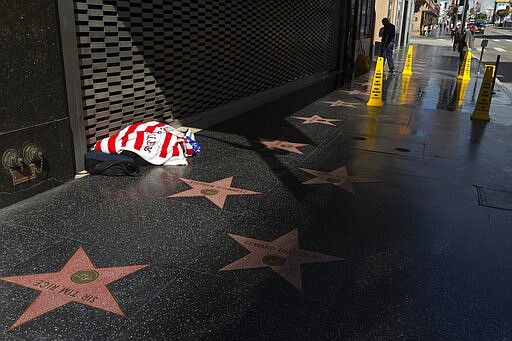 Workers clean the sidewalk of the closed Hollywood Pantages Theatre, as a homeless person sleeps under a blanket on the Hollywood Walk of Fame in Los Angeles on Tuesday, March 24, 2020. (AP Photo/Damian Dovarganes)