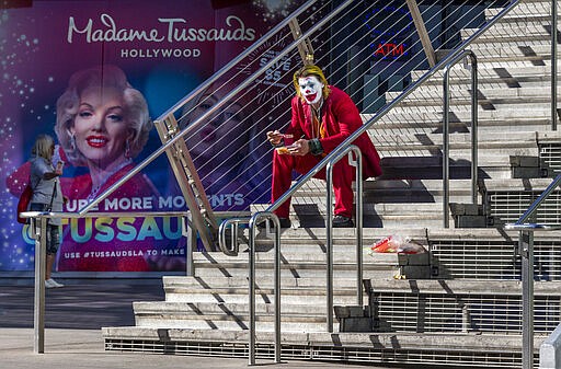 A street performer dressed as the Joker sits to eat on the steps of the closed Madame Tussauds Hollywood wax museum, a tourist destination on Hollywood Boulevard in Los Angeles on Tuesday, March 24, 2020. (AP Photo/Damian Dovarganes)