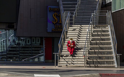 A street performer dressed as the Joker sits to eat his lunch on the steps of the closed Madame Tussauds Hollywood wax museum, a tourist destination on Hollywood Boulevard in Los Angeles on Tuesday, March 24, 2020. (AP Photo/Damian Dovarganes)