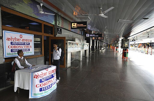 FILE- In this Monday, March 23, 2020, file photo, an Indian railways employee sits at a coronavirus help desk at the deserted New Delhi Railway station during a lockdown amid concerns over the spread of Coronavirus, in New Delhi, India. India's colossal passenger railway system has come to a halt as officials take emergency measures to keep the coronavirus pandemic from spreading in the country of 1.3 billion. The lifeline was cut Sunday, leaving hundreds of people stranded at railway stations, hoping to be carried onward by buses or taxis that appeared unlikely to arrive. The railway system is often described as India's lifeline, transporting 23 million people across the vast subcontinent each day, some 8.4 billion passengers each year. (AP Photo/Manish Swarup)