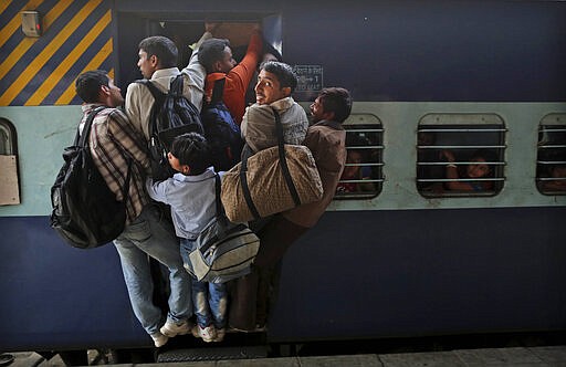 FILE - In this Friday, Nov. 16, 2012, file photo, Indians hang out from an overcrowded train to travel home for the Chhath Puja festival dedicated to the Sun God, at a railway station in New Delhi, India. India's colossal passenger railway system has come to a halt Sunday, March 22, 2020, as officials take emergency measures to keep the coronavirus pandemic from spreading in the country of 1.3 billion. The railway system is often described as India's lifeline, transporting 23 million people across the vast subcontinent each day, some 8.4 billion passengers each year. (AP Photo/Kevin Frayer, File)