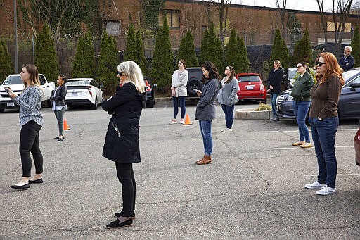 In this March 16, 2020, photo, staff of &quot;Food and Friends,&quot; a food distribution service for people with life-challenging illnesses, practice social distancing by standing a clear distance apart as they listen to District of Columbia Mayor Muriel Bowser speak about the city's response to the coronavirus during a news conference in Washington. (AP Photo/Jacquelyn Martin)