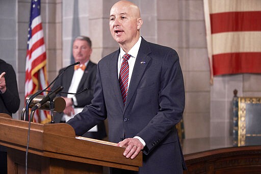 In this March 20, 2020 photo, Neb., Gov. Pete Ricketts speaks during a press briefing on the coronavirus in Lincoln, Neb., as Jim Macy, Director of the Nebraska Department of Environment and Energy, left, maintains social distancing. All participants in the news conference held on to the lectern. (AP Photo/Nati Harnik)