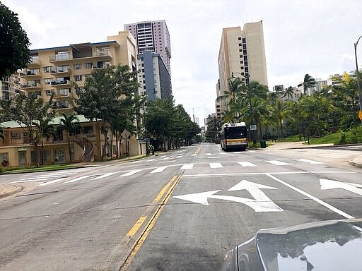 A city bus is parked on an empty street in the Waikiki neighborhood of Honolulu, Thursday, March 26, 2020. A 14-day quarantine on travelers takes effect in Hawaii, one of the world's most famous tourist destinations, as the island state fights the coronavirus. Hawaii welcomed 10 million travelers last year, for an average of about 830,000 a month. Authorities expect this number will dwindle to nearly zero in April as the new rule is implemented. Dozens of hotels are temporarily shutting their doors in response. (AP Photo/Caleb Jones)