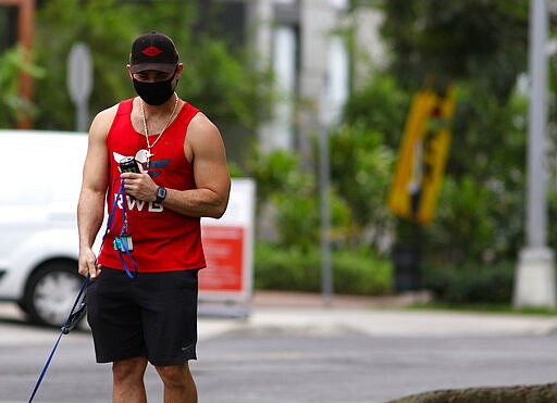 A man walks a dog in Honolulu, Thursday, March 26, 2020. A 14-day quarantine on travelers takes effect in Hawaii, one of the world's most famous tourist destinations, as the island state fights the coronavirus. Hawaii welcomed 10 million travelers last year, for an average of about 830,000 a month. Authorities expect this number will dwindle to nearly zero in April as the new rule is implemented. Dozens of hotels are temporarily shutting their doors in response. (AP Photo/Caleb Jones)