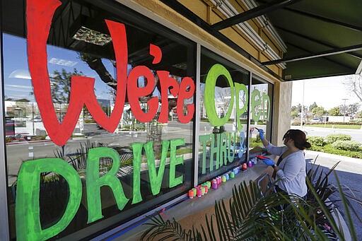 Lucy Kwak paints a sign on the window of a fast food chain's restaurant indicating that the drive-thru window is still open as well as a takeout optionduring the coronavirus outbreak in Garden Grove, Calif., Thursday, March 26, 2020. (AP Photo/Chris Carlson)