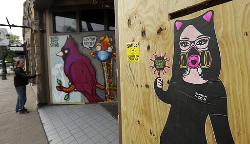 A man looks at coronavirus related art on boarded up businesses on 6th Street in Austin, Texas, Wednesday, March 25, 2020. Austin is under Stay at Home orders to help battle the spread of COVID-19, the disease caused by the new virus.  (AP Photo/Eric Gay)