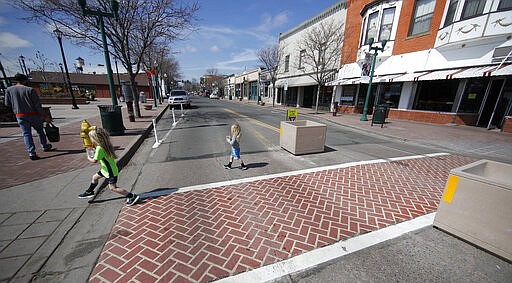 Two girls runs across the main street as they follow their father after he picked up a food order from a restaurant as a statewide stay-at-home order takes effect to reduce the spread of the new coronavirus Thursday, March 26, 2020, in Arvada, Colo. The new coronavirus causes mild or moderate symptoms for most people, but for some, especially older adults and people with existing health problems, it can cause more severe illness or death. (AP Photo/David Zalubowski)