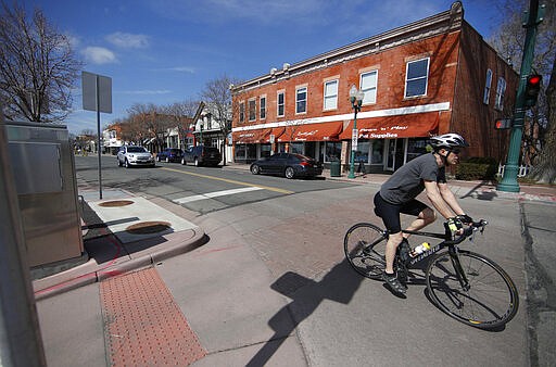 A bicyclist rolls down the empty main street as a statewide stay-at-home order takes effect to reduce the spread of the new coronavirus Thursday, March 26, 2020, in Arvada, Colo. The new coronavirus causes mild or moderate symptoms for most people, but for some, especially older adults and people with existing health problems, it can cause more severe illness or death. (AP Photo/David Zalubowski)