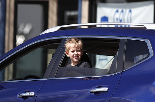 A young boy sticks his heads out of the rear window of a sports-utility vehicle while waiting for a pickup order outside a restaurant as a statewide stay-at-home order takes effect to reduce the spread of the new coronavirus Thursday, March 26, 2020, in Arvada, Colo. The new coronavirus causes mild or moderate symptoms for most people, but for some, especially older adults and people with existing health problems, it can cause more severe illness or death. (AP Photo/David Zalubowski)