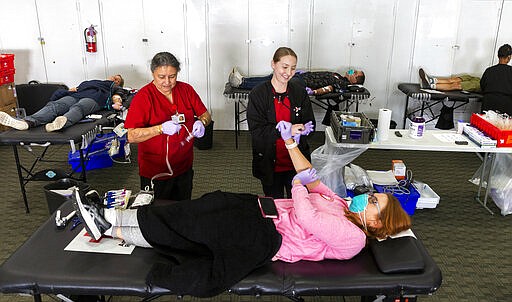 Registered Dietitian, Sheri Weitz, from Westchester, Calif., wears a face mask and gloves, as she donates blood with her husband, Gary &quot;Robin&quot; Wietz, seen in background, center, at the American Red Cross office in Santa Monica, Calif., Thursday, March 26, 2020. The new coronavirus causes mild or moderate symptoms for most people, but for some, especially older adults and people with existing health problems,  it can cause more severe illness or death. (AP Photo/Damian Dovarganes)