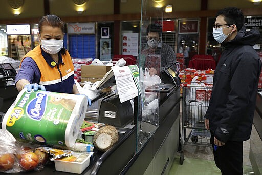 A cashier, left, works behind a plexiglass shield at a Super H Mart grocery store in Niles, Ill., Thursday, March 26, 2020. Local grocery stores are installing plexiglass shields in the checkout aisle as a coronavirus precaution. (AP Photo/Nam Y. Huh)