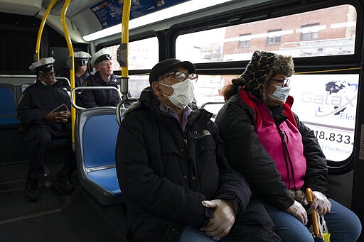 Passengers wear masks while riding a city bus during the coronavirus pandemic, Wednesday, March 25, 2020 in the Brooklyn borough of New York. Police have stepped up efforts to pressure New Yorkers to practice social distancing at the epicenter of the crisis. It's part of a global challenge that law enforcement and health officials say is critical to containing the coronavirus. (AP Photo/Mark Lennihan)