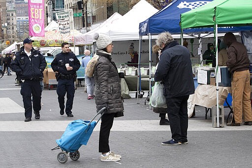 A shopper stands on a social distancing marking as police officers patrol the farmers market in Union Square, Wednesday, March 25, 2020, in New York. Police have stepped up efforts to pressure New Yorkers to practice social distancing at the epicenter of the crisis. It's part of a global challenge that law enforcement and health officials say is critical to containing the coronavirus. (AP Photo/Mary Altaffer)