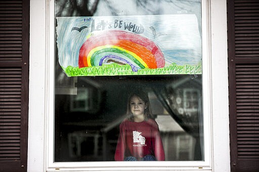 Kate Madsen, 6, displays her drawing in her window in hopes that it would cheer her neighbors up on Wednesday, March 25, 2020 in Sioux Falls, S.D. Madsen and her first-grade classmates are learning remotely to prevent the spread of the coronavirus at Robert Frost Elementary School. The six-year-old says she misses her teachers, friends and art class. (Abigail Dollins/The Argus Leader via AP)