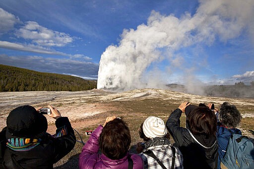 FILE - In this May 21, 2011 file photo, tourists photograph Old Faithful erupting on schedule late in the afternoon in Yellowstone National Park, Wyo. On Tuesday, March 24, 2020 the National Park Service announced that Yellowstone and Grand Teton National Parks would be closed until further notice, and no visitor access will be permitted to either park..(AP Photo/Julie Jacobson, File)